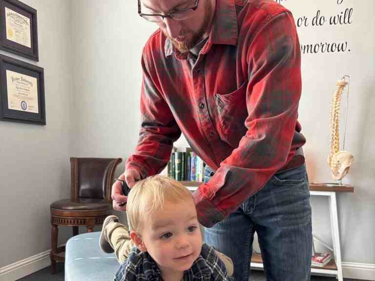 Reviews 2 Child receiving chiropractic adjustment with a chiropractor in an exam room for pediatric spinal health and wellness.